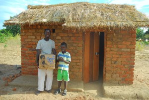 two Malawai boys standing in front of a hut holding a Manna Pack