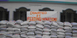 in fornt pf Mercy and Grace Building, a sign above dozens of bags of food says, " Donated by Feeding The Nations"