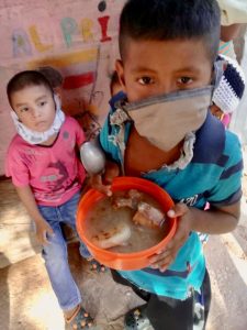 a photo of a little boy with the mask holding a bowl full food.